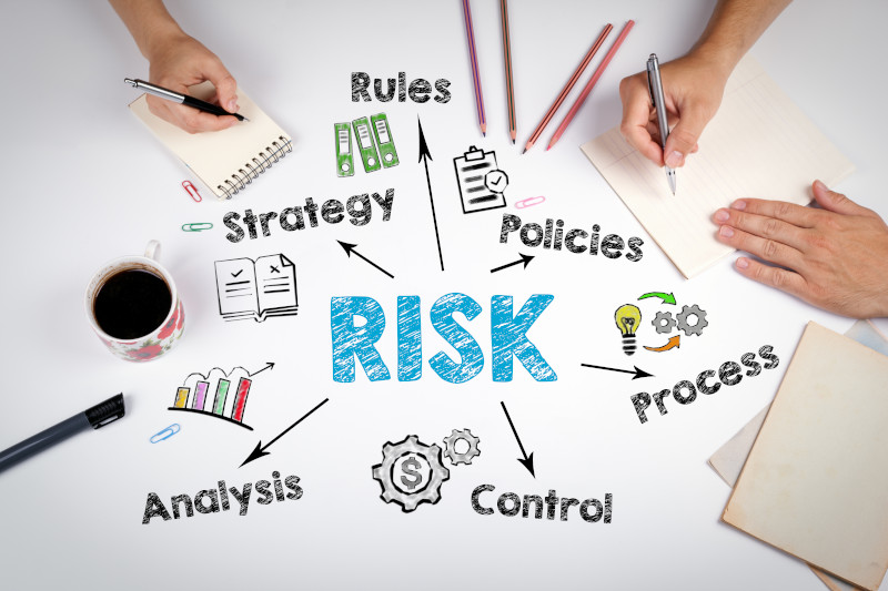 Photo of tabletop with hands and notepads with overlaid illustration of the word risk linking out to other words (rules, strategy, analysis, policies, process and control).